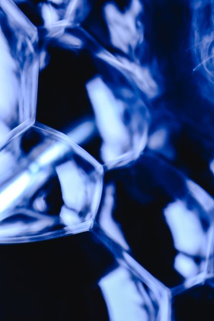 Close-up image of several faceted, irregularly shaped crystal or glass objects with a reflective, shiny surface, primarily in shades of blue and silver. The objects are clustered together, creating a textured appearance with highlights and shadows that emphasize their geometric forms. The background is dark, allowing the reflective surfaces of the crystals or glass to stand out prominently, capturing light and creating a visually striking composition. This image represents the detailed, reflective qualities often associated with packaging or decorative items used in home relocations or moving processes, illustrating the importance of careful packing and handling during furniture transport and packing and moving services offered by companies like Man with Van Colindale.