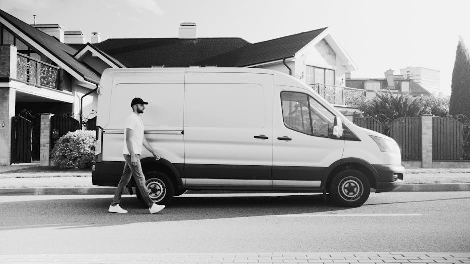 A row of six white commercial vans parked closely together on a paved surface, with rear doors visible and some showing black window frames. The vans are positioned with their backs facing the camera,