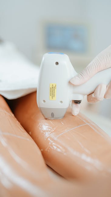 A close-up image showing a person wearing a white glove using a handheld device to perform a therapy or treatment on a person's leg, which is covered in transparent gel. The setting appears clinical with a blurred background including a wall-mounted monitor or screen. The scene suggests a professional health or wellness procedure, possibly related to physical therapy or medical treatment, with an emphasis on precision and care. This image could relate to the broader context of comprehensive home relocation services provided by Man with Van Colindale, highlighting the importance of professional handling, precise logistics, and care during furniture transport and packing processes for house removals in the NW9 area.